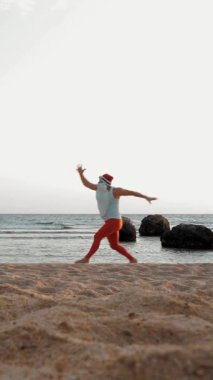 Komik Noel Baba. Deniz kenarındaki Noel Baba. Noel Baba acele ediyor. Tişörtlü ve kırmızı taytlı Noel Baba deniz kıyısında koşar. sıcak yaz günü.