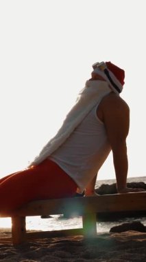 Komik Noel Baba güneşleniyor. Noel Baba deniz kıyısındaki tahta şezlongda uzanır. Güneşin doğuşunda dinlenir. Noel Baba yaz tatilinde, deniz kıyısında..