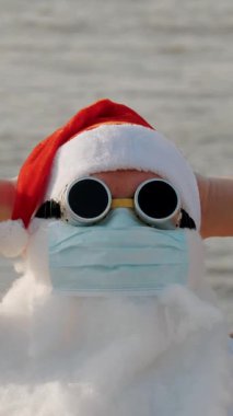Koruyucu maskeli komik Noel Baba. Noel Baba, güneş gözlükleriyle sahilde güneşleniyor, dinleniyor. Coronavirus salgını sırasında Noel Baba tatili ya da deniz kıyısında tecrit..