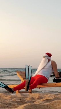 Komik Noel Baba güneşleniyor. Noel Baba, güneş gözlüğü ve palet takmış, deniz kıyısında, dinleniyor ve müzik dinliyor, dinleniyor. Noel Baba yaz tatilinde, deniz kıyısında..