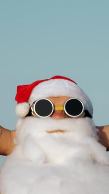 Noel Baba yaz tatili. Portre. Noel Baba güneşleniyor. Komik Noel Baba, güneş gözlüklü, deniz kenarında, palmiye ağaçlarına yaslanmış, dinleniyor..