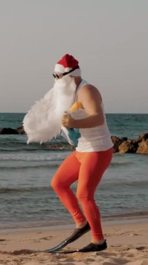 Noel Baba yaz tatili. Noel Baba eğleniyor. Güneş gözlüklü ve paletli komik Noel Baba, sahilde dans ediyor ve dinleniyor. Noel Baba şnorkelle dalacak
