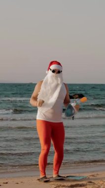 Noel Baba yaz tatili. Noel Baba eğleniyor. Güneş gözlüklü ve paletli komik Noel Baba, sahilde dans ediyor ve dinleniyor. Noel Baba şnorkelle dalacak