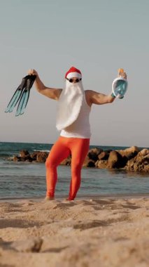 Noel Baba yaz tatili. Noel Baba eğleniyor. Komik Noel Baba, güneş gözlüklü, yüzgeçli ve şnorkelli, deniz kenarında dans ediyor. Noel Baba şnorkelle dalacak