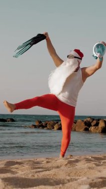 Noel Baba yaz tatili. Noel Baba eğleniyor. Komik Noel Baba, güneş gözlüklü, yüzgeçli ve şnorkelli, deniz kenarında dans ediyor. Noel Baba şnorkelle dalacak