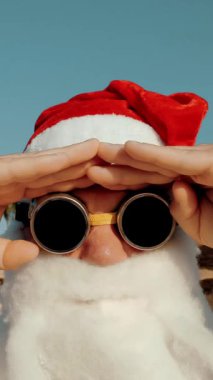 Noel Baba yaz tatili. Noel Baba eğleniyor. Komik Noel Baba, güneş gözlüklü, deniz kenarında, palmiye ağaçlarının önünde. Noel Baba selfie çeker. Noel Baba blogcusu.