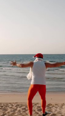 Noel Baba yaz tatili. Noel Baba eğleniyor. Komik Noel Baba, paletlerle kumlu sahilden denize koşuyor. Yüzmek için acele ediyor, şnorkel. arka plan