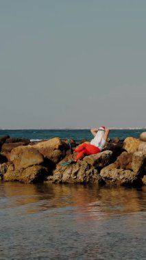 Noel Baba güneşleniyor. Noel Baba eğleniyor. Komik Noel Baba, güneş gözlüğü ve yüzgeçleriyle deniz kıyısındaki kayalık sahilde oturuyor. Noel Baba yaz tatili
