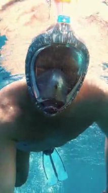 Adam şnorkelle yüzüyor. Bir yüzücü, şnorkel maskesi takmış, denizde şnorkelle yüzüyor ve su altında fotoğraf makinesiyle selfie çekiyor. Güneş ışığı suyun yüzeyini aydınlatır..