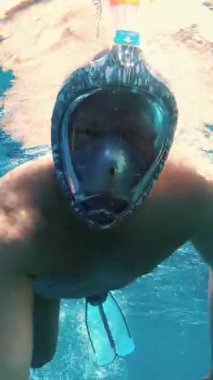 Adam şnorkelle yüzüyor. Bir yüzücü, şnorkel maskesi takmış, denizde şnorkelle yüzüyor ve su altında fotoğraf makinesiyle selfie çekiyor. Güneş ışığı suyun yüzeyini aydınlatır..