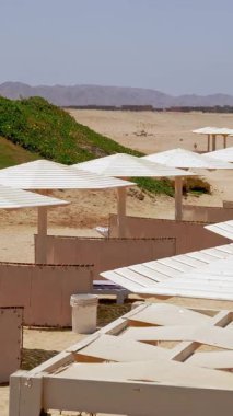 Güneş şemsiyeleri. Plaj sandalyeleri. Şemsiyeli ve güneşli kumlu boş kumsallar. Kızıl Deniz kıyısında. Sıcak yaz günü