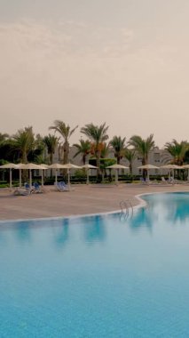 Yüzme havuzu, palmiye ağaçları, güneş şemsiyeli güneşlikler. Tropikal manzara. Otel kompleksinin bölgesi..