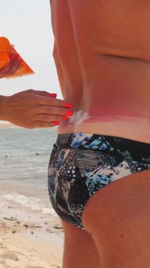 Güneş kremi. Güvenli bronzlaşma. Güneş yanığı. Zararlı güneş radyasyonuna karşı koruma. Yakın plan. Kadın, erkeğin vücuduna güneş kremi sürüyor. Sahilde, denizde. Güneşli sıcak bir gün