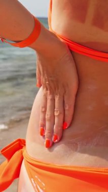 Güneş kremi. Güvenli bronzlaşma. Güneş yanığı. Zararlı güneş radyasyonuna karşı koruma. Yakın plan. Kadın eli vücut derisine güneş kremi sürer. Sahilde, denizde. Güneşli sıcak bir gün