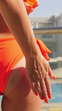 Güneş kremi. Güvenli bronzlaşma. Güneş yanığı. Zararlı güneş radyasyonuna karşı koruma. Yakın plan. Kadın eli vücut derisine güneş kremi sürer. Yüzme havuzunun arka planı. Güneşli sıcak bir gün