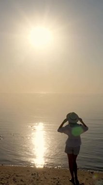 Denizin üzerinde şafak. Denizin üzerinde güneşin doğuşuna hayran olan genç bir kadının silueti. Yaz sabahı.