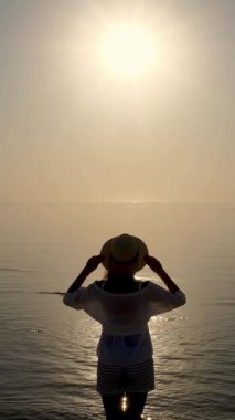 Denizin üzerinde şafak. Denizin üzerinde güneşin doğuşuna hayran olan genç bir kadının silueti. Yaz sabahı.