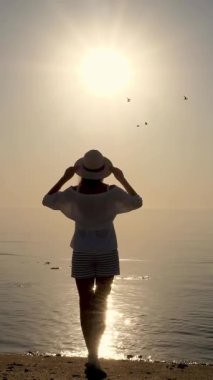 Denizin üzerinde şafak. Denizin üzerinde güneşin doğuşuna hayran olan genç bir kadının silueti. Yaz sabahı.