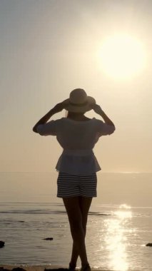 Denizin üzerinde şafak. Denizin üzerinde güneşin doğuşuna hayran olan genç bir kadının silueti. Yaz sabahı.