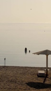 Denizde sakinim. Denizin üzerinde şafak. Denizde yüzen iki insan silueti. Boş güneş şezlongları ve güneş şemsiyeleriyle ıssız bir sahil. Yaz sabahı