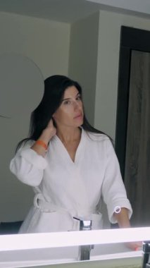 Aynanın önündeki kadın. Beyaz bornozlu güzel bir kadın aynanın önünde dikiliyor ve yansımasını inceliyor.