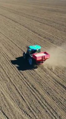 Büyük tekerlekler üzerinde tarım traktörü havadan görünümü verimli çiftlik alanı boyunca sürmek, tohum matkap ile mineral gübre yayılan, sürülmüş zemin üzerinde büyük toz yükseltir. Bahar toprak ekimi