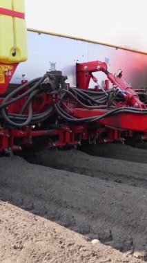 Yakın plan, makineleşmiş patates ekme işlemi. Özel teçhizatlı büyük traktör, uzun düz üst sıraları, çizgileri, tepecikleri, yeni ekilmiş patatesleri, ekilen siyah toprak tarlasında, bahar günü, ekim mevsiminde.