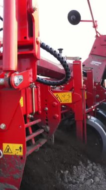 Yakın plan, makineleşmiş patates ekme işlemi. Özel teçhizatlı büyük traktör, uzun düz üst sıraları, çizgileri, tepecikleri, yeni ekilmiş patatesleri, ekilen siyah toprak tarlasında, bahar günü, ekim mevsiminde