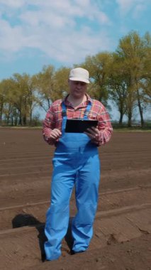 Çiftçi, ziraatçi tarlada toprak sıraları arasında duruyor, ekicinin patates ekme kalitesini test ediyor. Modern tarım. Bahar güneşli gün.