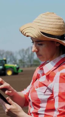 CHERKASY, UKRAINE, APRIL 28, 2020: Kadın çiftçi, tarım uzmanı çiftlikte duruyor. Test ediyor, tablet kullanıyor, ekicinin patates ekme kalitesini ölçüyor. Modern tarımsal olarak patates yetiştirme. Bahar güneşli gün.