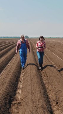 Çiftçi ve tarımcı, tarladaki toprak sıraları arasında, tabletle, ekicinin patates ekme kalitesini test ederek derin bir çizgide yürüyor. Modern tarım. Bahar güneşli gün.