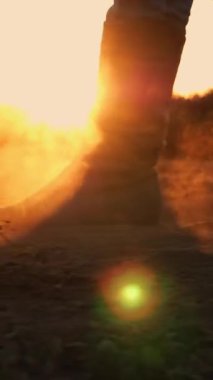 Çizmeli çiftçi tarlada yürüyor. Yakın plan. Çiftçilik botları içinde bacaklar. Tozlu, toprak. Gün batımında arka ışıklandırma. Taze sürülmüş tarım arazisi. Alt görünüm