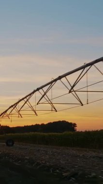 Çiftlik arazisinde gün batımı. Günbatımında tarla tarlası. Gün batımında sulama sistemi olan tarımsal bir tarla boyunca tozlu toprak bir yol..