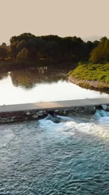 Şelaleden bir Weir 'ın hava görüntüsü. Küçük Barajı olan Huzurlu Nehir, Yeşillik ile çevrili. Gün batımında nehrin üzerinde beton köprü.