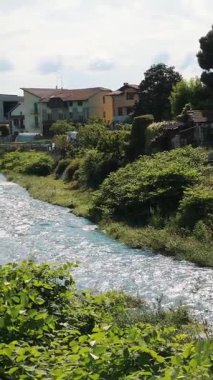 Kayalık akarsu yatağı ile akan dağ nehri yeşil bankaların ve yaz güneşinin altında konut evlerinin yanında akar.