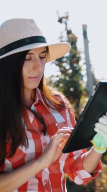 Elma hasadı. Tabletli çiftçi. Hasat teftişi. Kadın tarım uzmanı dijital tablet kullanıyor, işçiler meyve bahçesinden elma topluyor. Bahçıvanlıkta, çiftçilikte modern teknoloji. Tarım teknolojisi.