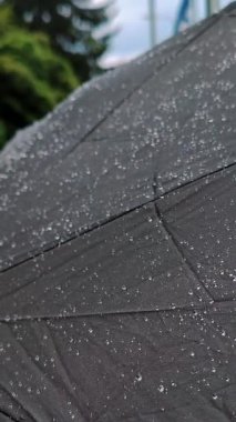 Şemsiyenin üzerine yağmur damlaları. Siyah şemsiye, yağmur damlaları, yağmurlu hava. Yazın, Avrupa 'da bulutlu gökyüzünün altında, yağmur yağıyor. Arka planda, bir nehir ve bir Avrupa şehri.