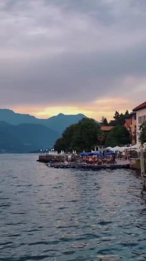 Alplerde bir göl. Göl kıyısında bir kasaba, bir sürü kafesi olan bir gezinti güvertesi. Turistler için bir tekne istasyonu. Gün batımında dağlar