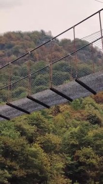 Alp dağları arasında yeşil bir ormanda, bir dağ nehri üzerindeki uzun asma köprü. İtalya. Yaz günü. Yaz boyunca yağmur ve bulutlu hava.