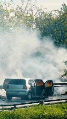 Acil müdahale ekibi güneşli bir günde yol kenarındaki bir araba yangınına katılıyor.