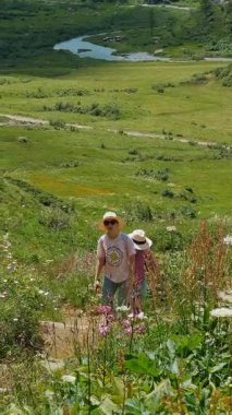Sırt çantalı iki yürüyüşçü, yemyeşil tepeler ve kır çiçekleriyle çevrili dar bir patika boyunca seyahat ederler..