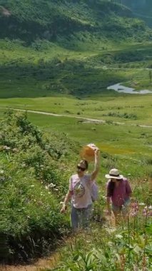 Sırt çantalı iki yürüyüşçü, yemyeşil tepeler ve kır çiçekleriyle çevrili dar bir patika boyunca seyahat ederler..