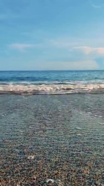 Yazın şafakta kumsalda. Deniz ve dalgalar, mavi bir arkaplan şeffaf bir gökyüzü. Deniz çakılı.