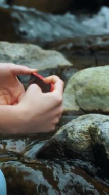 Ormanda Alplerdeki bir dağ nehrinin kenarında doğayı fotoğraflayan bir kız.
