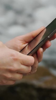 Bir kızın elindeki cep telefonunun yakın plan görüntüsü. Nehir kenarındaki ormanda yaz mevsimi. Bir rotayı kontrol ediyorum, haritayı inceliyorum. Turizm ve yürüyüş. Rahatlama.