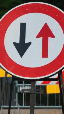 Trafik levhası. Sembol. Ters hareket. Yakın plan. Kırmızı ve siyah oklar yuvarlak kırmızı çerçeve işaretinde. Tamir çalışmaları yolda devam ediyor. Arkaplanda kırmızı bant olan çit.