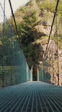 Uzun ve boş asma köprü bir dağ nehri üzerinde Alp dağları arasında yeşil bir ormanda. İtalya. Yaz günü. manzaralı güzellik.