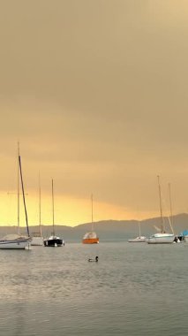 Yatçılık. Peyzaj. Gölün üzerinde gün batımı. Dağlardaki muhteşem göl manzarası. Birçok yelkenli yat ve tekne marinada demirlidir. bulutlu bahar havası.