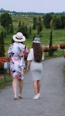 İki kız, turist, parkta romantik bir ara sokakta yürüyorlar. Bahçe düzenleme, çiçek tasarımı. Çiçek açan petunyalar. Botanik Bahçesi. botanik bahçesi.