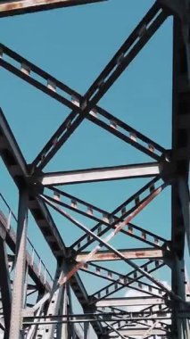 Metal köprü. Mavi gökyüzüne karşı kaba demir yapılar, hareket halindeki bir arabadan çekiliyor. Alt manzara. Nehrin karşısındaki demiryolu ve yol köprüsü. Çelik kirişleri aşan siluet.